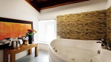 A modern bathroom with a freestanding bathtub, a wooden bench, and a stone wall.