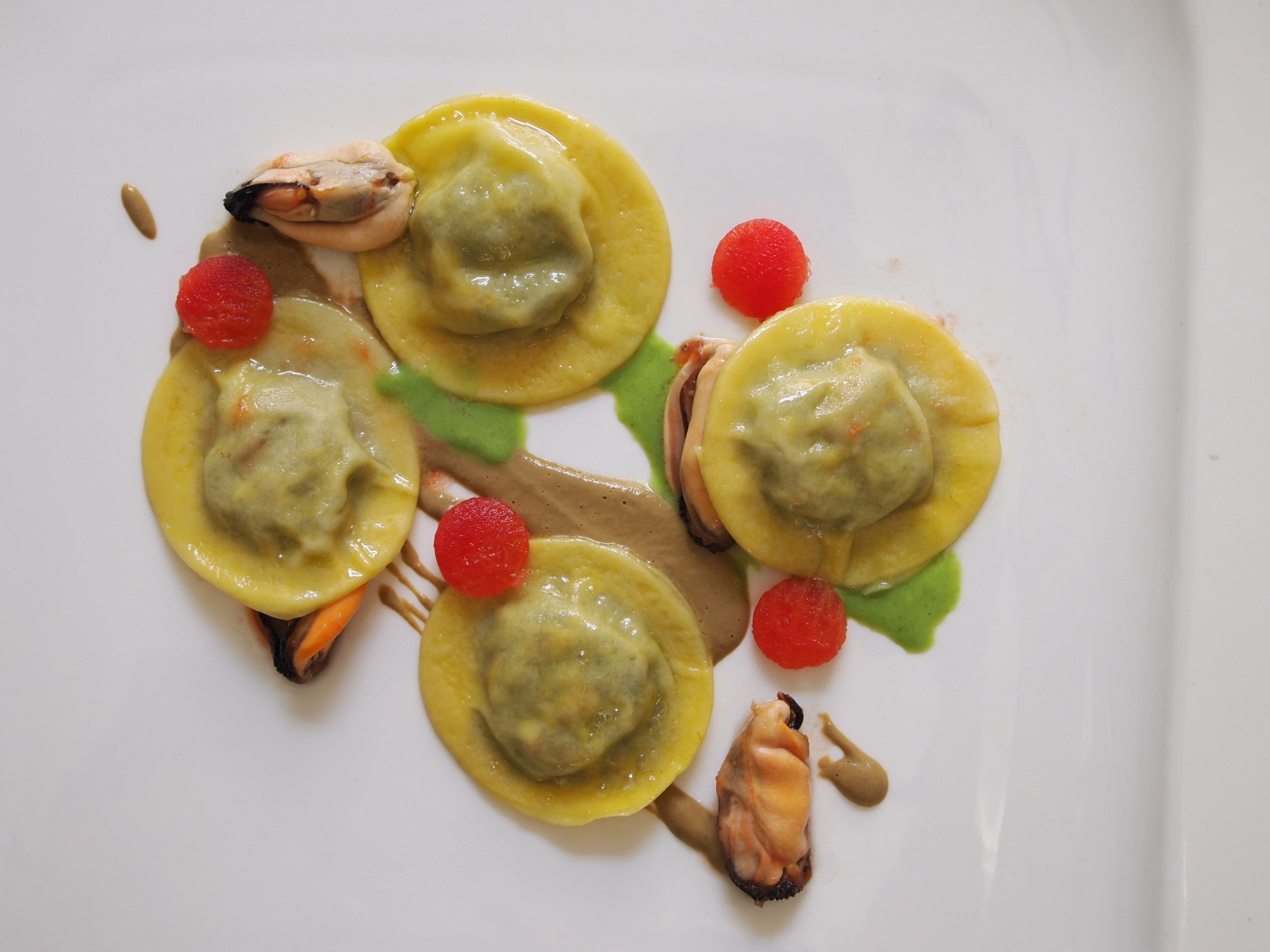 A plate with ravioli, garnished with red berries and a green leaf.