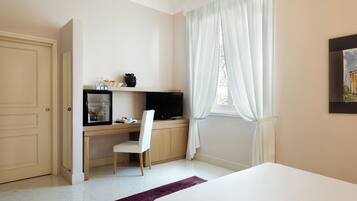 A hotel room with a bed, a desk with a computer, a chair, and a window with curtains.