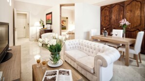 A modern living room with a white sofa, a wooden coffee table, and a dining area with a wooden table and chairs. - Palazzo Brunaccini Boutique Hotel (Palermo)