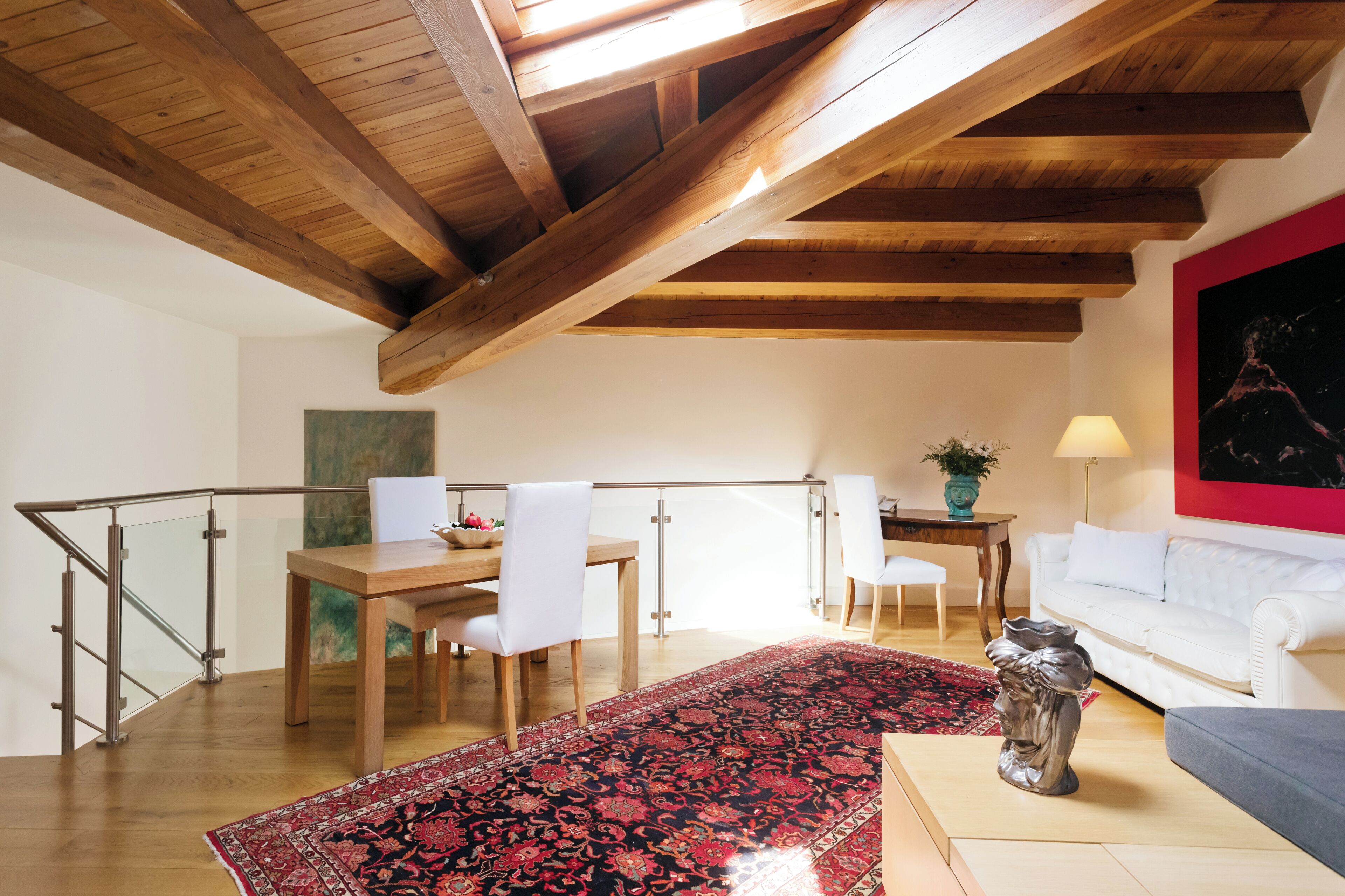 Ein geräumiger Wohnbereich mit Holzboden, einem Esstisch mit Stühlen, einer Couch, einem roten Teppich mit Muster und einer dekorativen Vase.