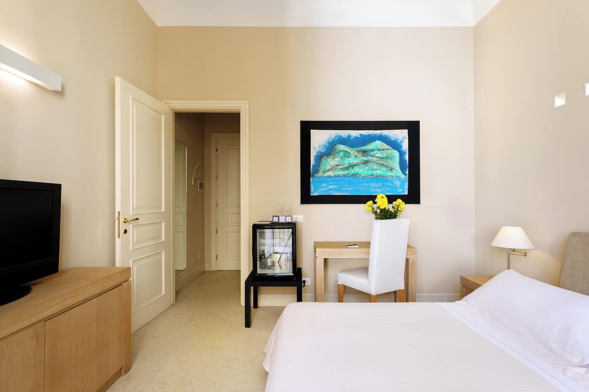 Une chambre d’hôtel avec un lit, un bureau, une chaise, une télévision et un tableau encadré au mur.