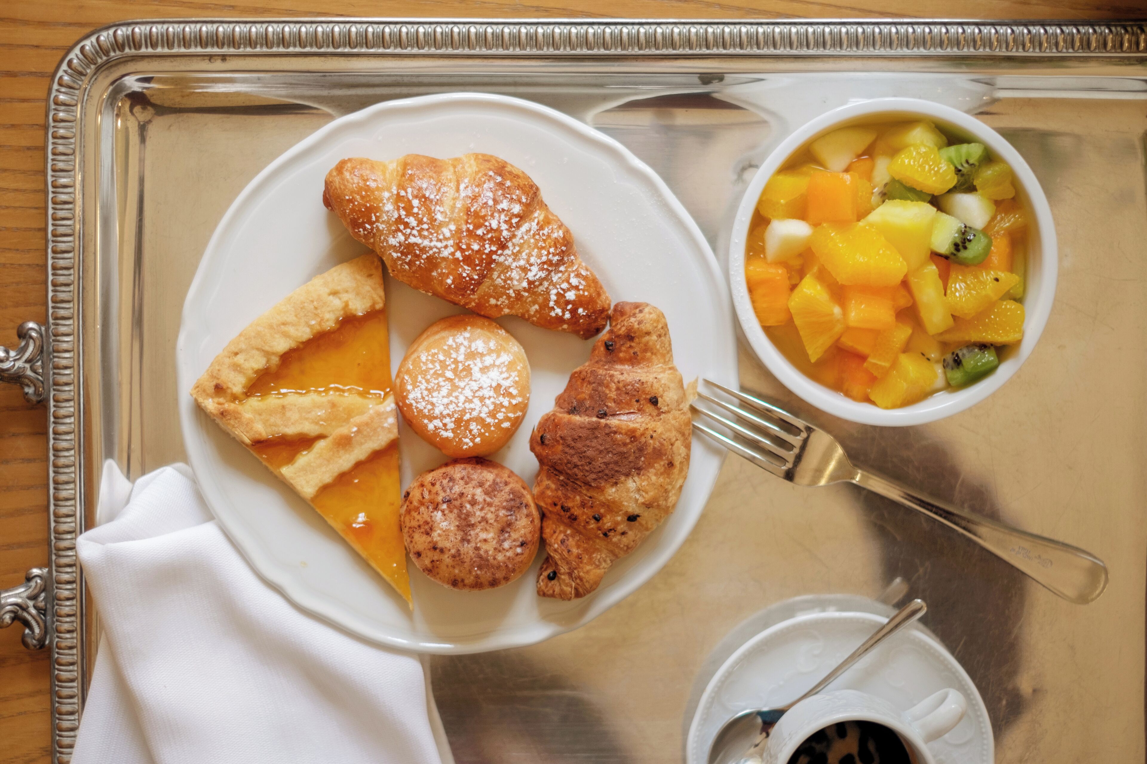A tray with a plate of pastries, a bowl of fruit, and a cup of coffee.