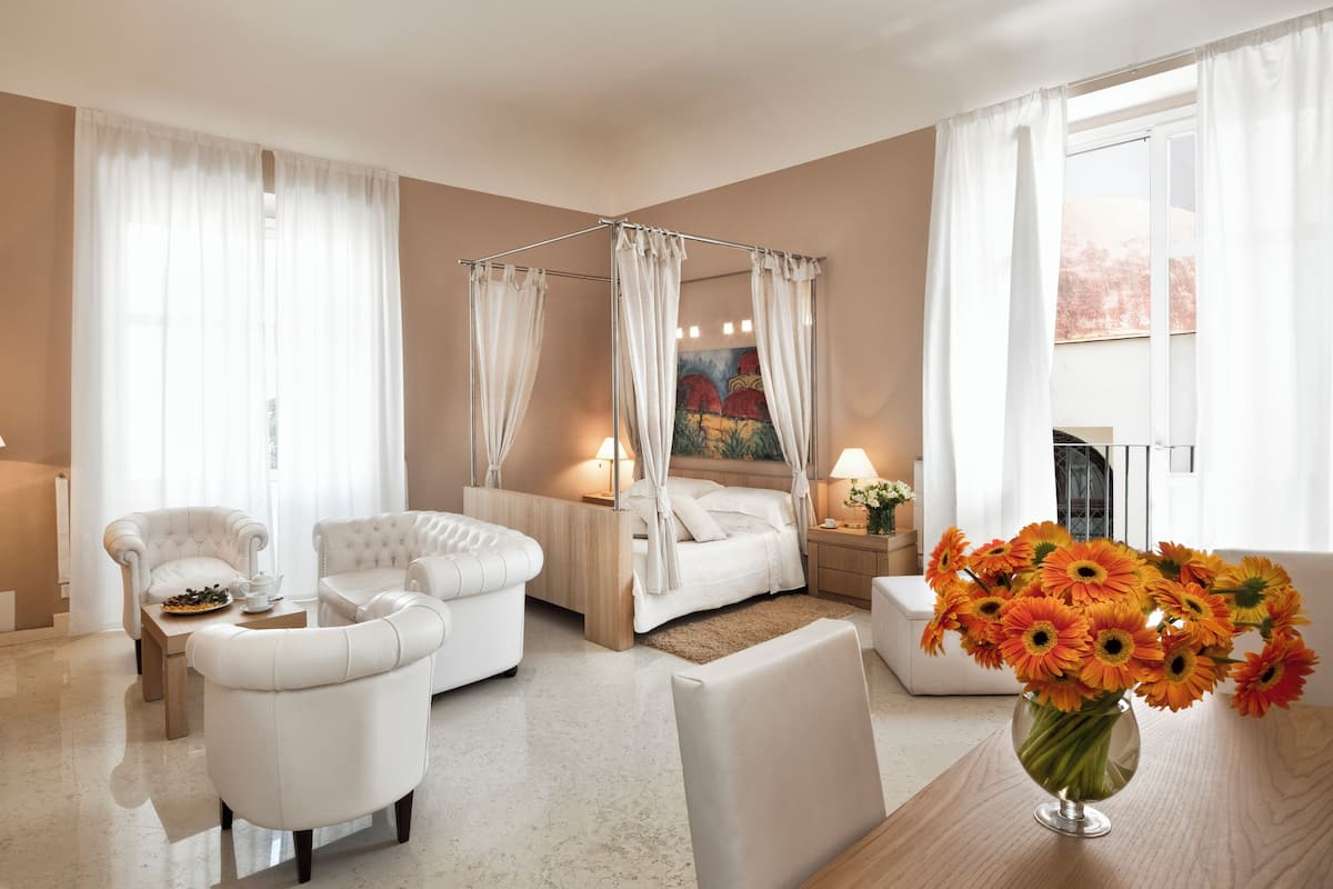 Une chambre d’hôtel avec un lit à baldaquin, deux fauteuils, une table basse, un téléviseur et un vase de fleurs.