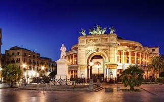Ein historisches Gebäude mit einem prunkvollen Eingang, einer Statue davor und klassischer Architektur.
