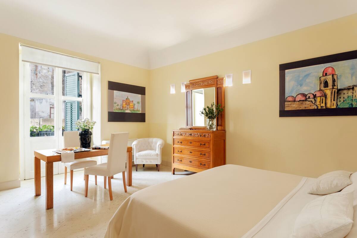Une chambre à coucher comprenant un lit, une commode, un bureau avec une chaise et une fenêtre avec des stores.