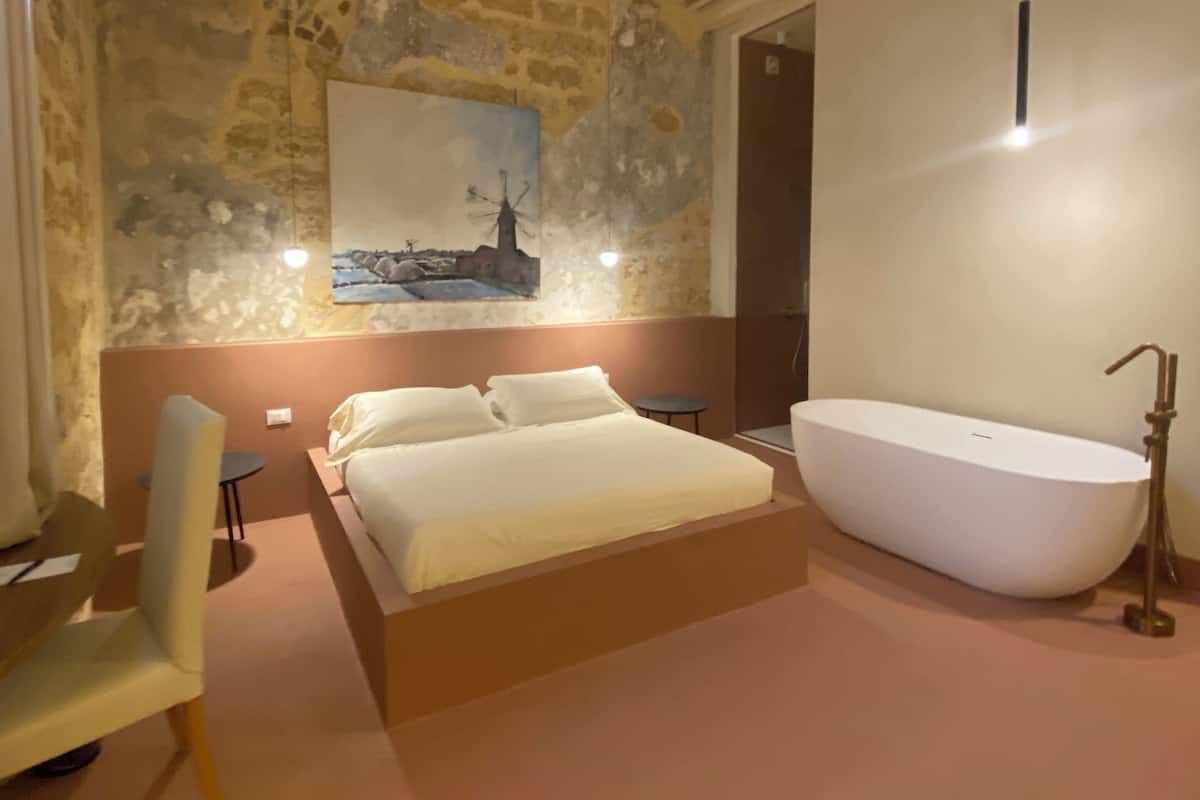 Une chambre avec un grand lit, une baignoire et un mur en pierre orné d’un tableau.
