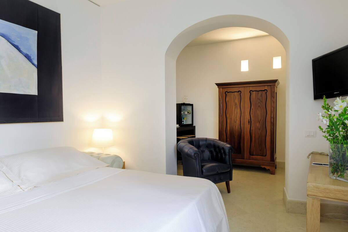 Une chambre d’hôtel avec un lit, une chaise, une armoire en bois et un téléviseur fixé au mur.