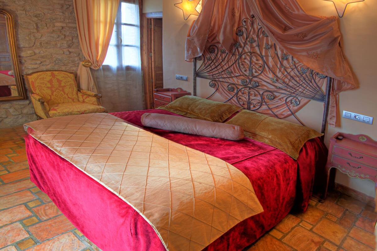 A bedroom with a four-poster bed, a stone wall, and a wooden ceiling.