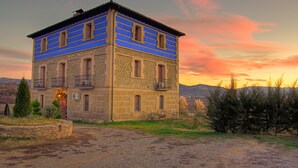 A two-story stone building with a blue facade, multiple windows, and a balcony. - Bodegas de Arnés - Adults Only (Graus)