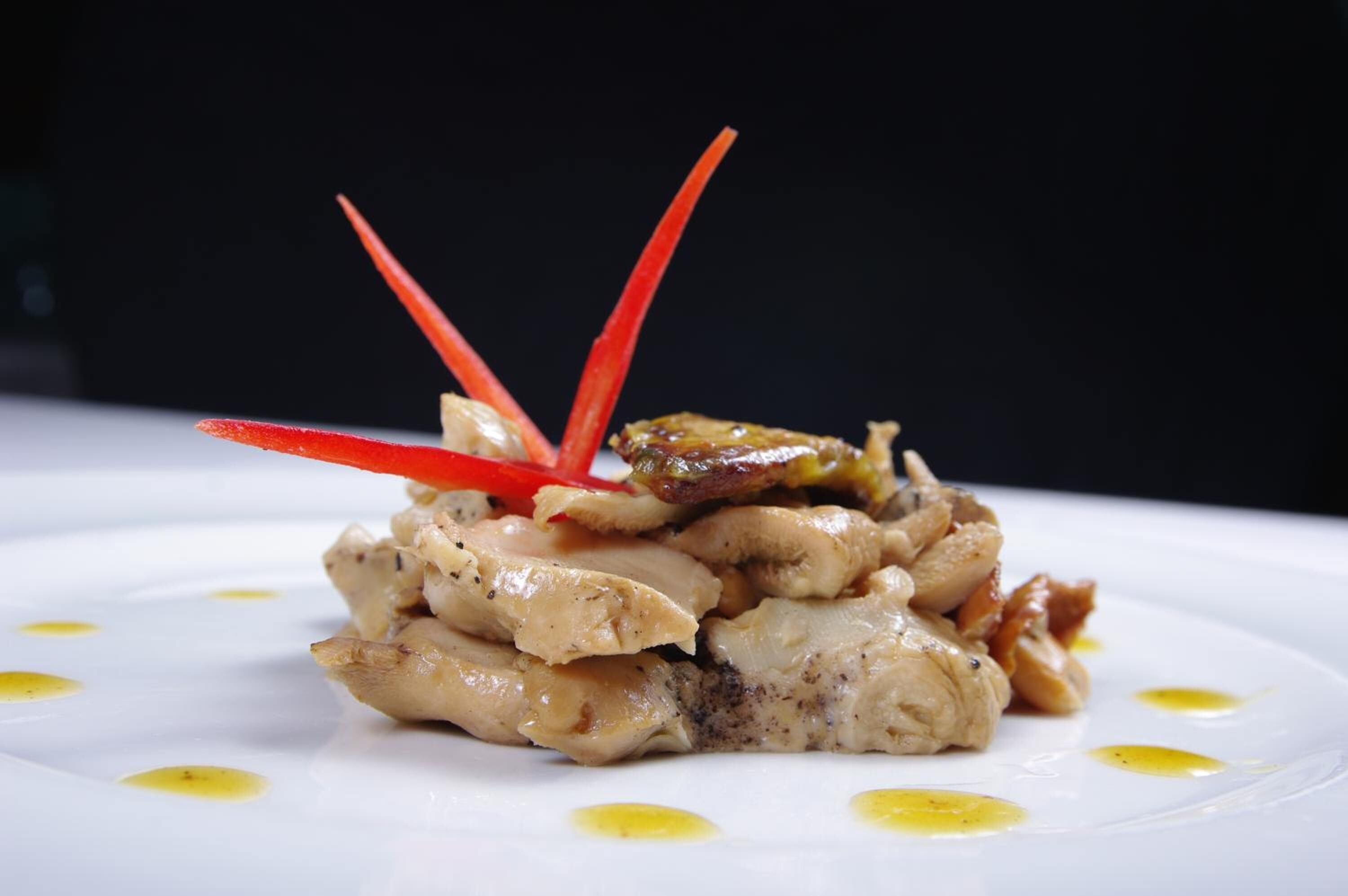 Un plato blanco con un guiso de pollo y verduras, adornado con palitos rojos.