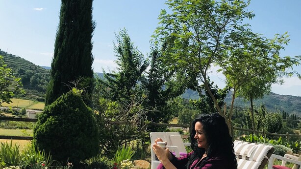 A person sitting on a striped lounge chair outdoors with a view of a hilly landscape and a tall tree in the background. - Bodegas de Arnés - Adults Only (Graus)