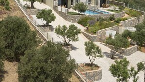 Une maison moderne à deux étages, dotée d’une piscine, entourée de jardins aménagés et bordée d’un paysage vallonné.
