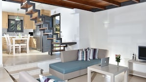 Un salon moderne avec un canapé, un coin repas avec des chaises, une cuisine équipée d’un réfrigérateur et un escalier menant à un autre niveau.