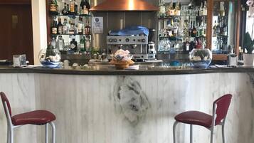 Angolo bar con un bancone in marmo, due sgabelli rossi, una macchina da caffè e scaffali pieni di bottiglie e bicchieri.