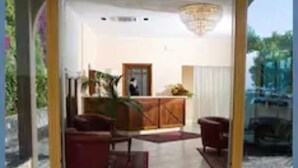 A hotel reception area with a reception desk, seating area, and a view of the outside. - Hotel Riviera Lido (Milazzo)