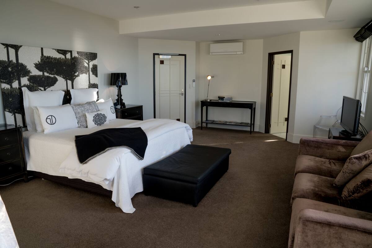 Une chambre moderne avec un grand lit, un banc noir, un bureau et un téléviseur.