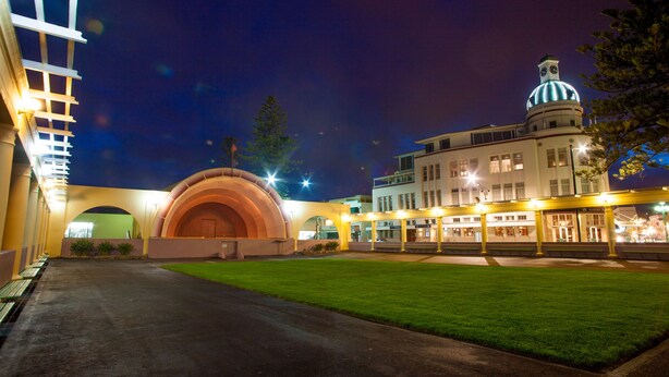 A building with a large arched entrance, a clock tower, and a well-lit facade at night.