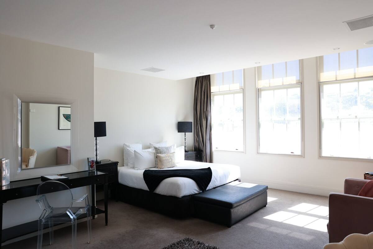 Une chambre d’hôtel moderne équipée d’un lit, d’un bureau, d’une chaise et de grandes fenêtres.