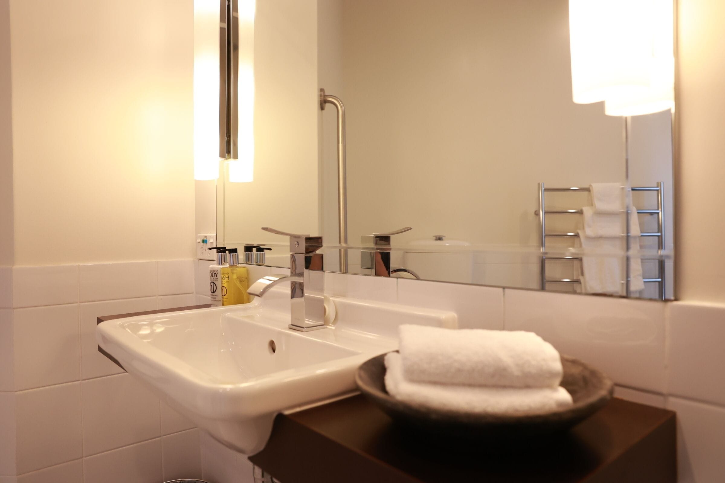 A modern bathroom with a white sink, a mirror, and a towel rack.