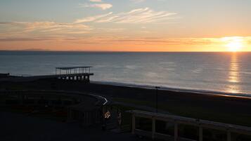 Vista costera con un atardecer sobre el agua, un muelle y un pequeño edificio con techo.