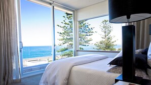 A hotel room with a bed, a lamp, and a view of the ocean.