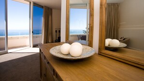 A room with a large window, a wooden dresser, a round ceramic bowl with three white spherical objects, and a mirror reflecting the room.