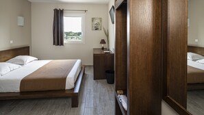 Quarto de hotel com duas camas, cabeceira de madeira, janela com cortinas, mesa de cabeceira com abajur e vista para o exterior.