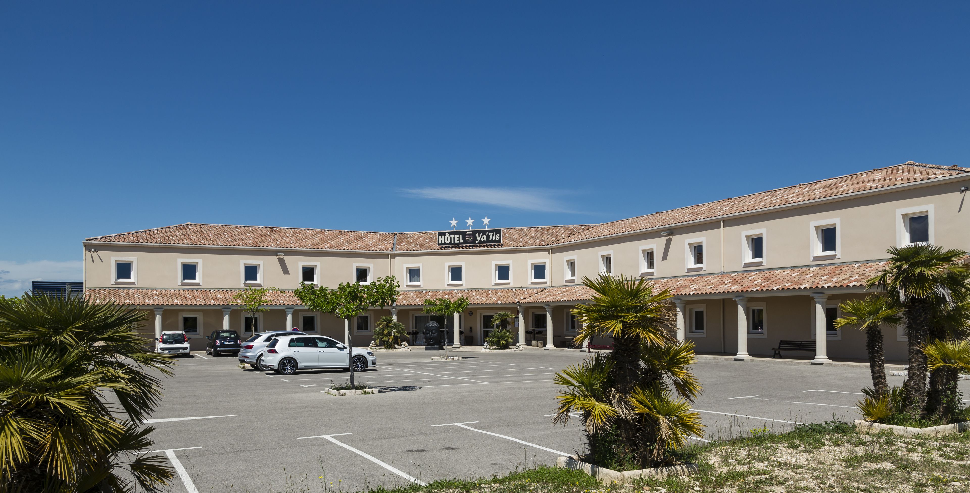 A hotel with a tiled roof, multiple windows, and a parking lot with several cars.