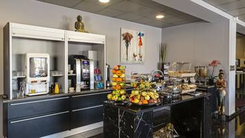 Een buffetgedeelte met diverse soorten fruit en drankjes, een koffieapparaat en een beeld op de balie.