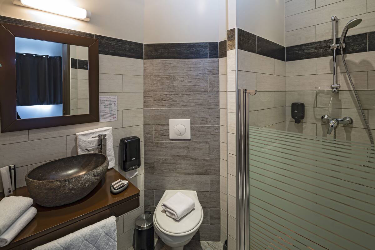 Een moderne badkamer met een grote wastafel, een toilet, een douche met glazen wand en een spiegel boven de wastafel.