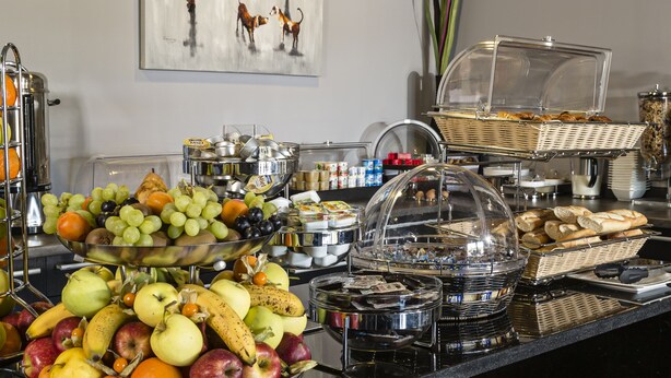 Um buffet com diversas frutas e doces, uma estátua e um quadro na parede.