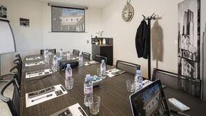 Uma sala de conferência com uma mesa comprida, cadeiras, laptops, garrafas de água e uma tela de projetor.