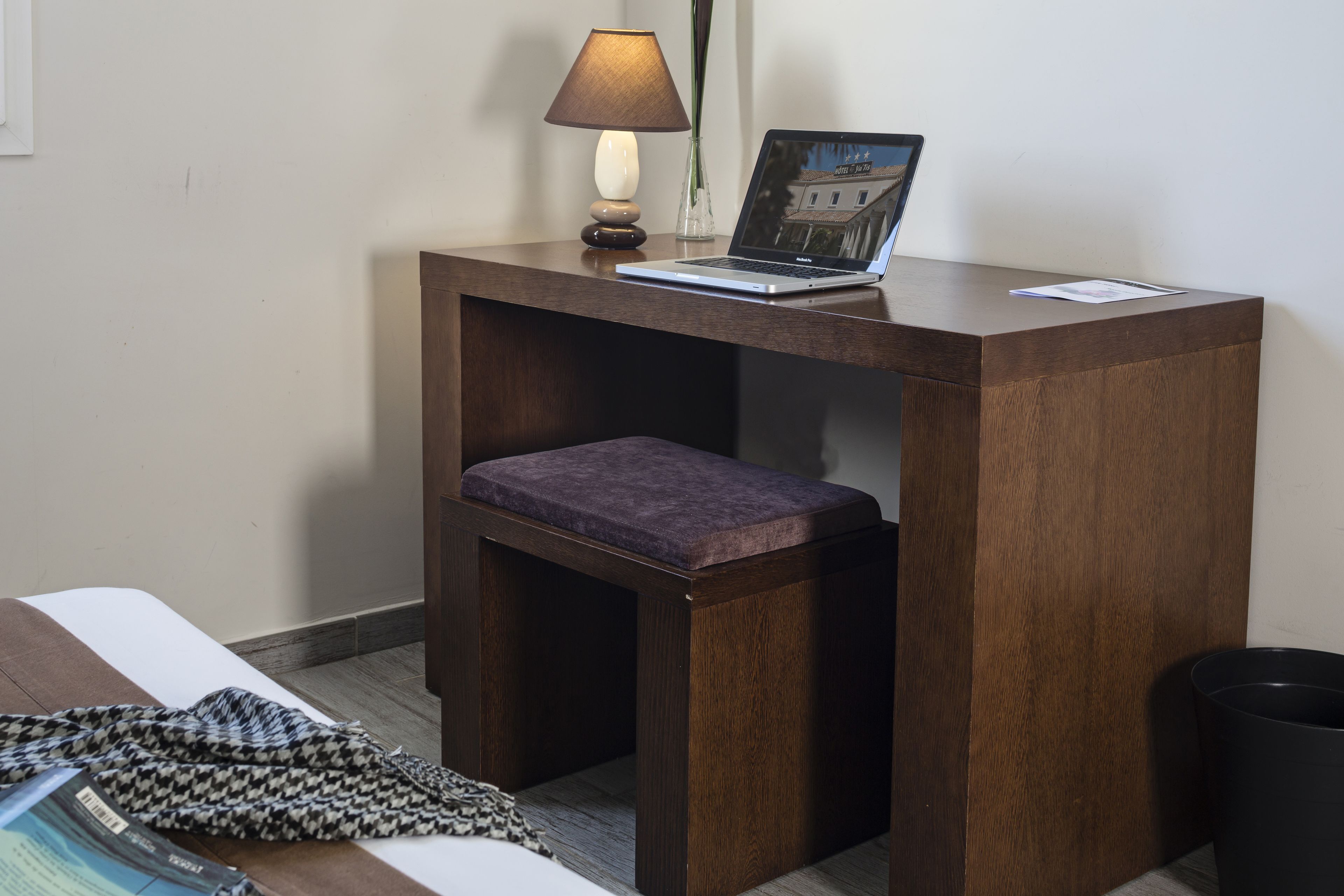 Ein kleiner Holztisch mit einem Laptop, einer Lampe und einer Vase.
