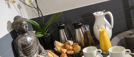 A breakfast setup with croissants, coffee, and juice, accompanied by a Buddha statue and orchids.