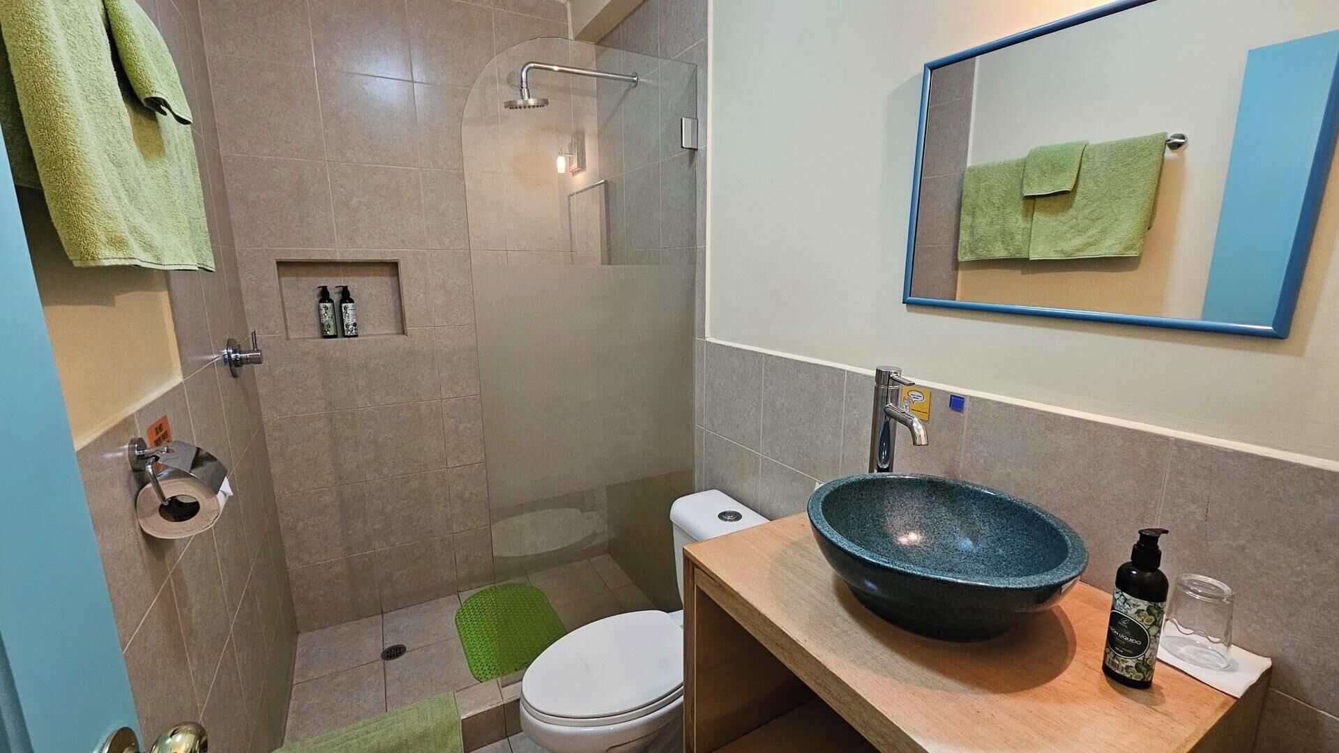 Un baño con ducha, inodoro, lavamanos y espejo.