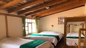 A room with three beds, wooden beams on the ceiling, and a green curtain. - Inti Sisa (Guamote)