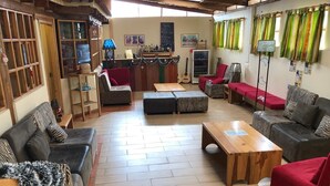 A cozy living area with a wooden floor, a red sofa, a black sofa, a zebra-patterned ottoman, and a wooden coffee table. - Inti Sisa (Guamote)