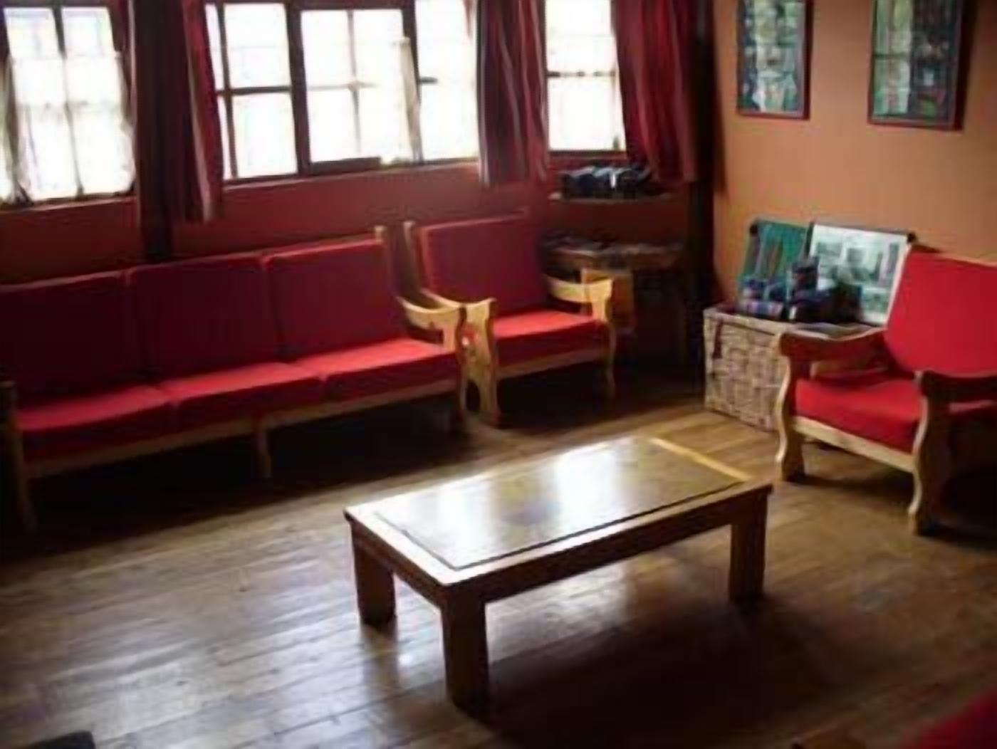 Quarto com piso de madeira, um sofá vermelho, uma mesa de centro de madeira e uma cadeira.