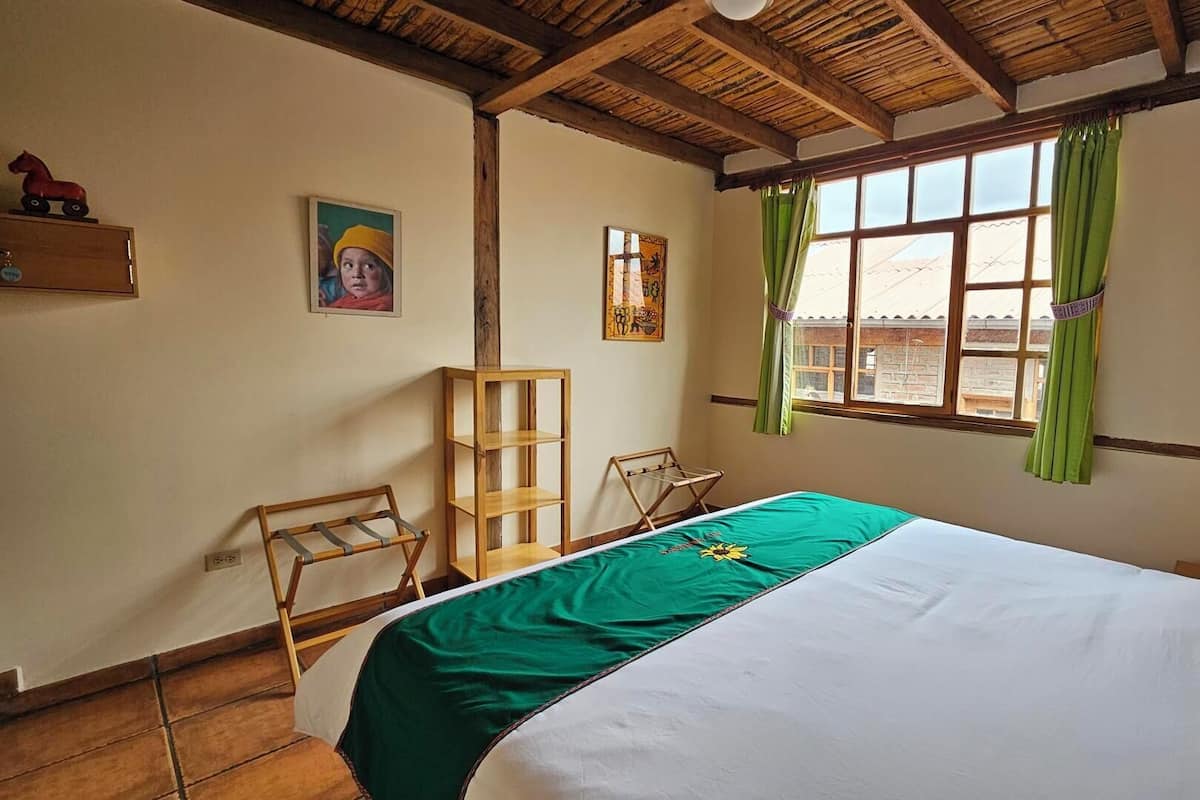 Quarto com cama, janela com cortinas verdes, prateleira de madeira e pintura na parede.