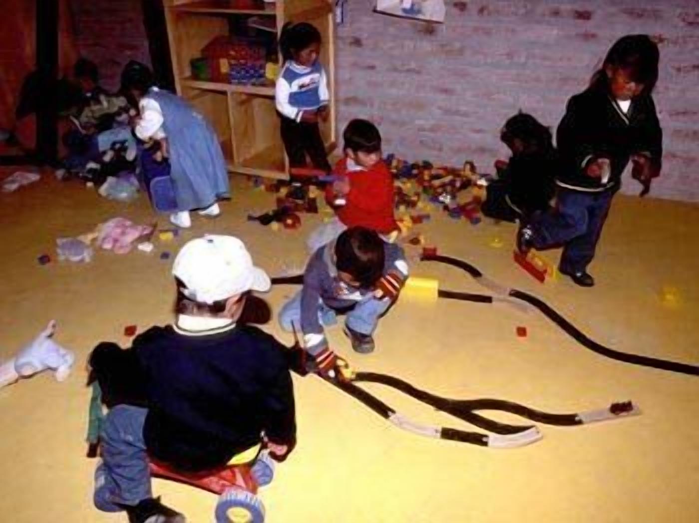 A group of children playing with toys in a room with a brick wall and wooden shelves.