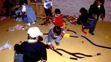 A group of children playing with toys in a room with a brick wall and wooden shelves.
