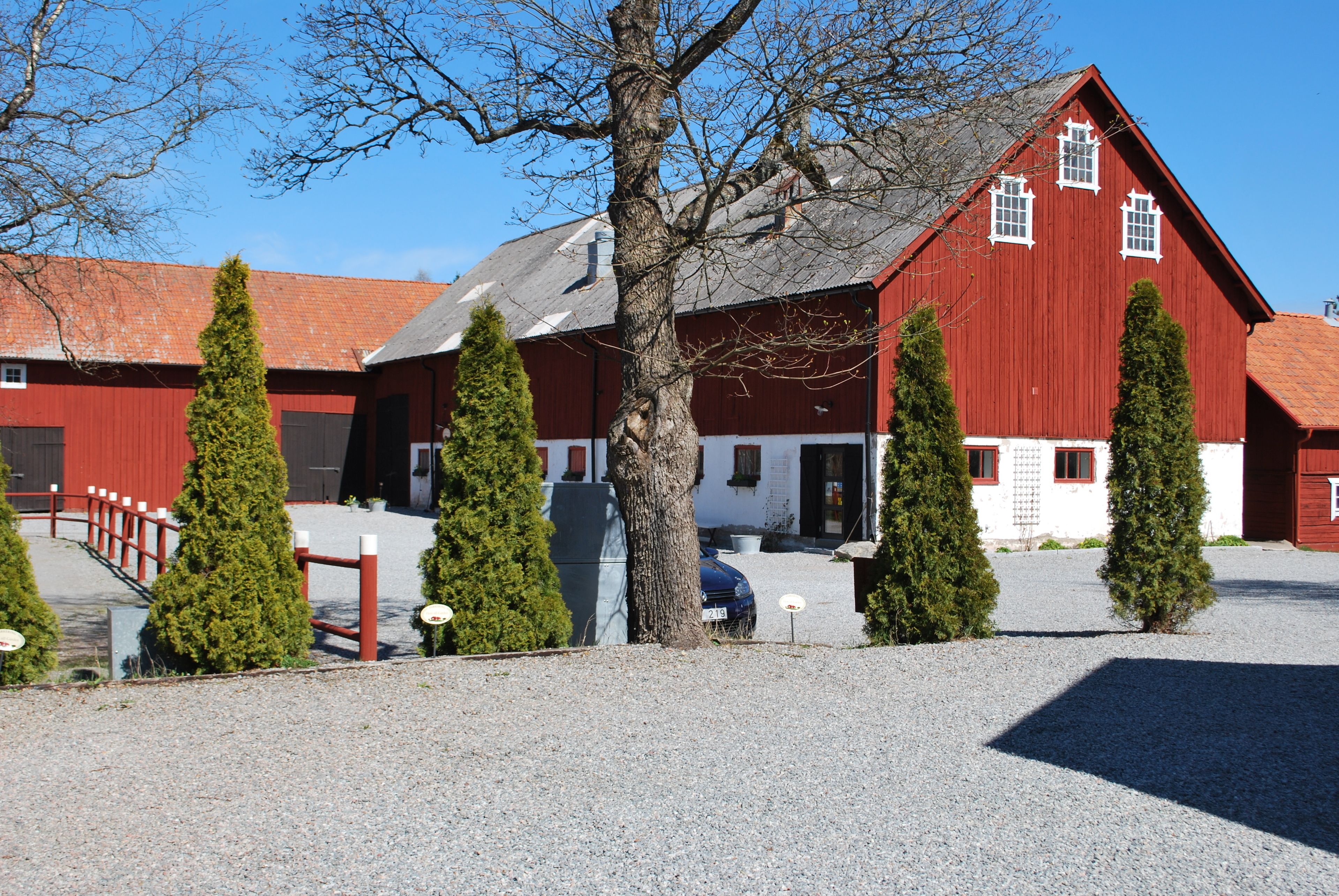 Ein rotes Bauernhaus mit einem Schotterweg und einem roten Zaun.