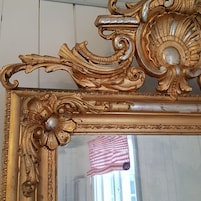 A gold-framed mirror with ornate designs and a reflective surface.