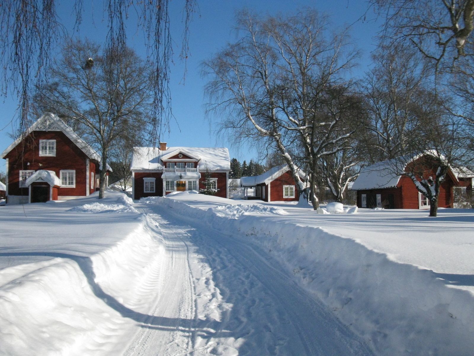 A snow-covered rural road leading to a row of red wooden houses with white trim.