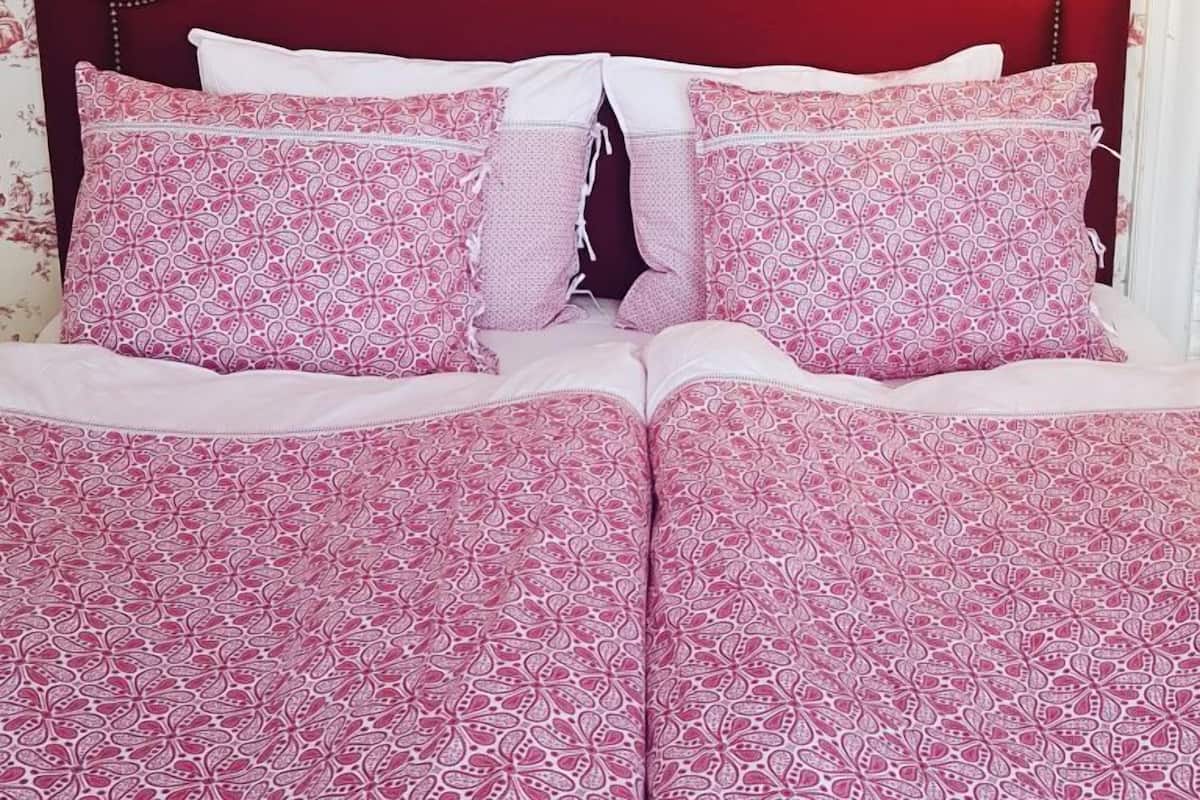 Ein Bett mit rotem Kopfteil, mehreren Kissen und einer gemusterten Tagesdecke.