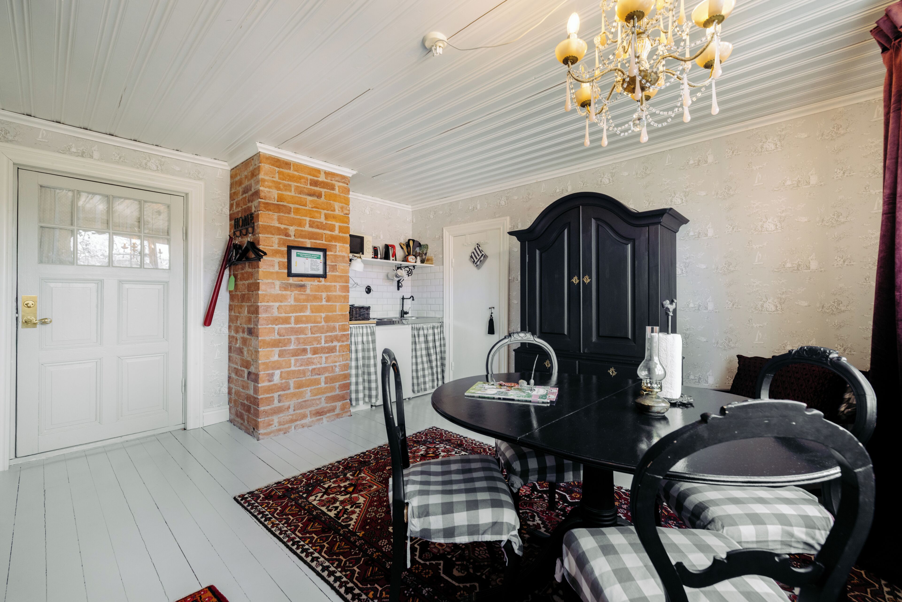 A dining area with a brick wall, a chandelier, and a black cabinet.