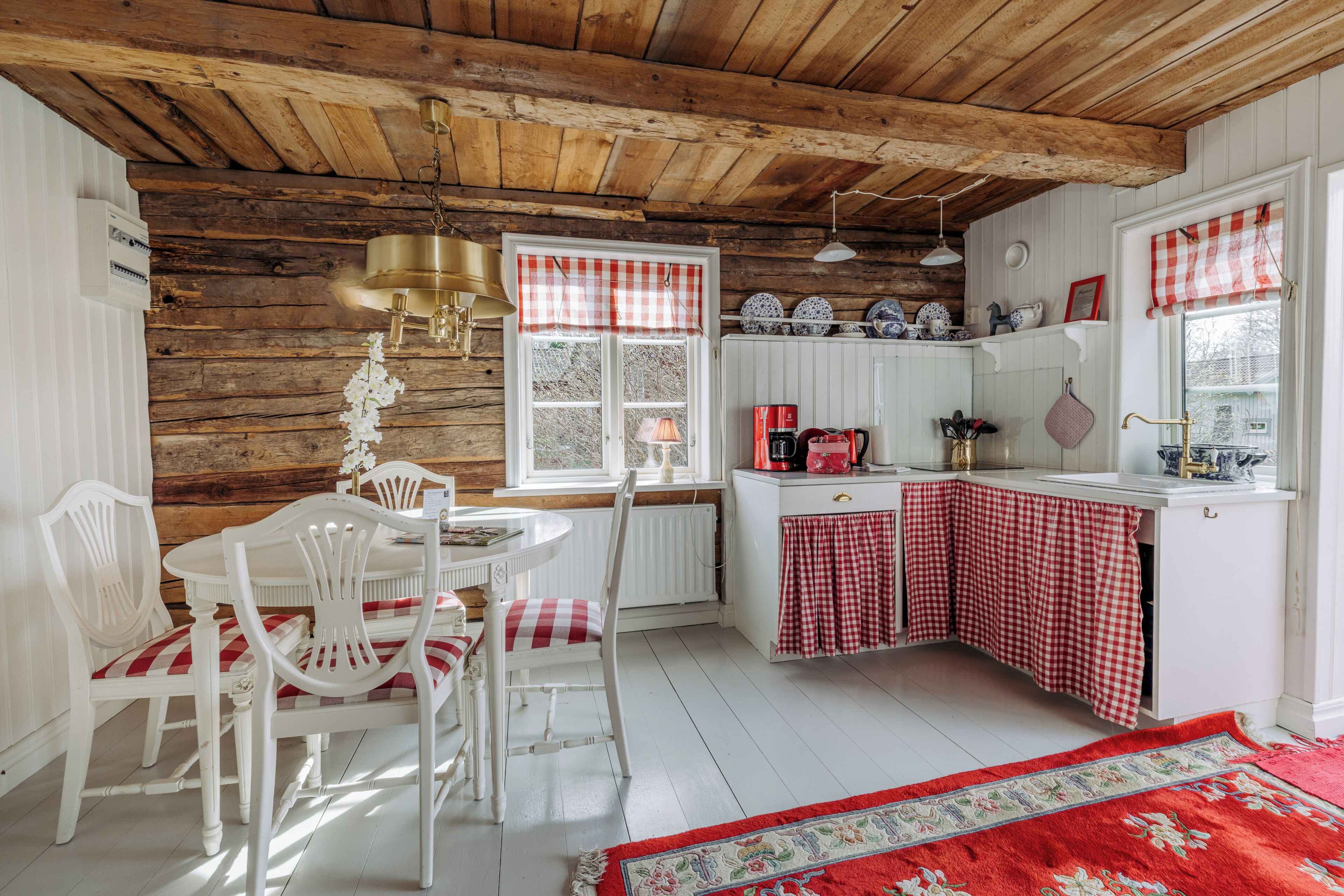A rustic kitchen with wooden beams, a white dining set, and a red and white checkered tablecloth.