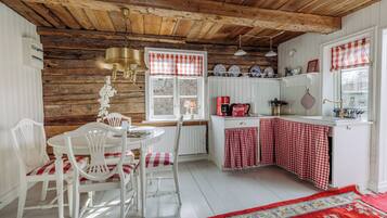A rustic kitchen with wooden beams, a white dining set, and a red and white checkered tablecloth.