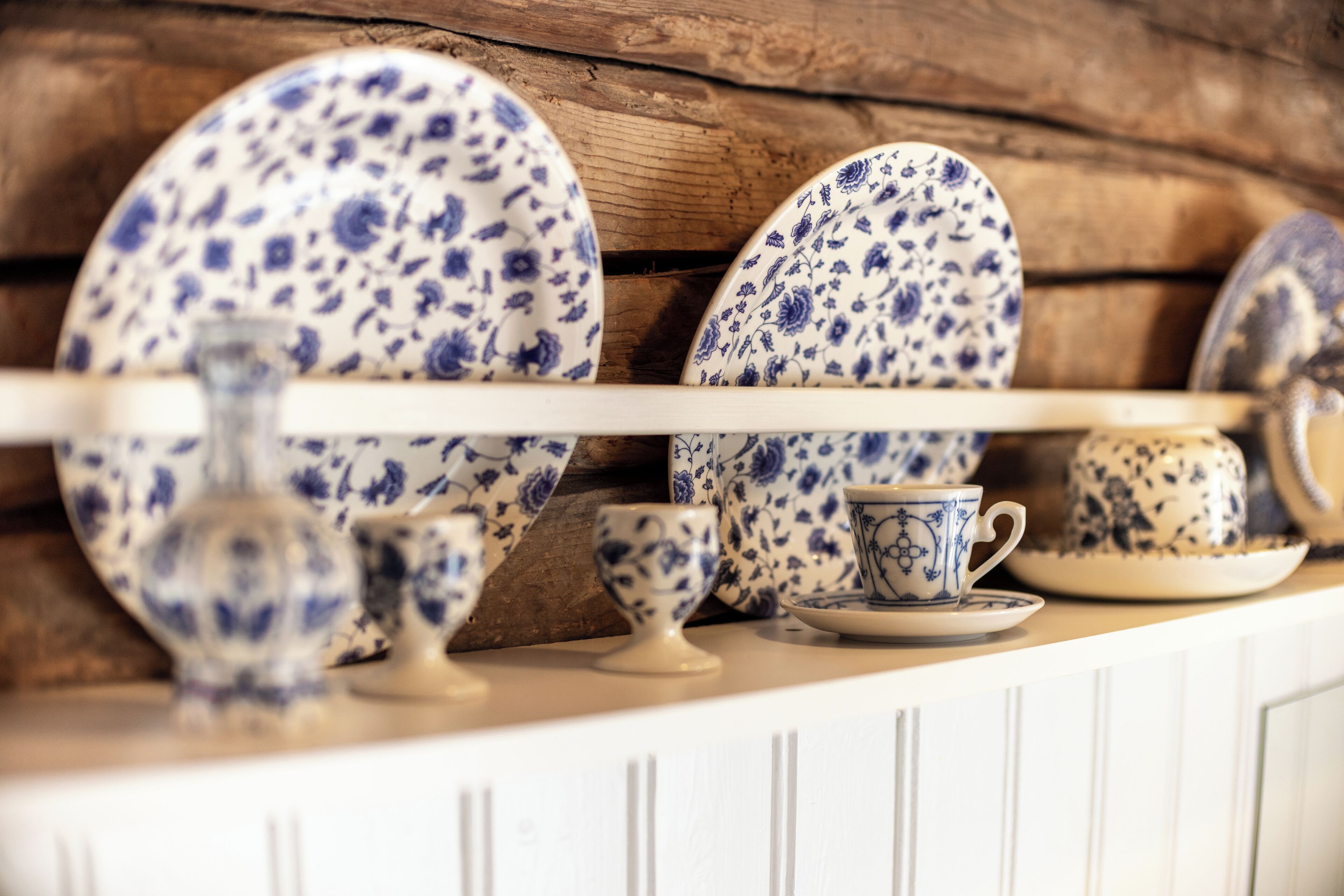 Una exposición de platos y tazas de cerámica con un estampado floral azul y blanco sobre una estantería de madera.